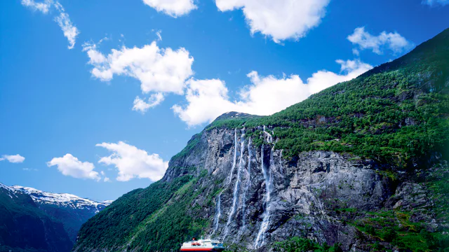 Bilden visar Hurtigrutens fartyg på håll framför vattenfallet sju systrar i Geirangerfjorden