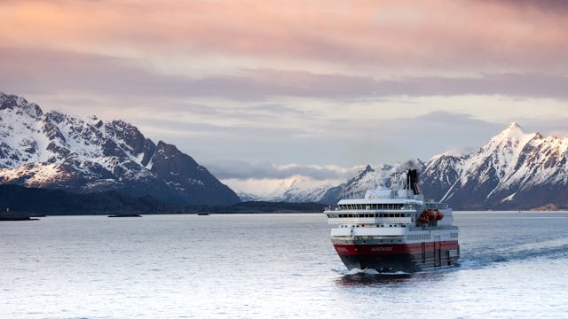 Bilden visar ett av Hurtigrutens fartyg i ett vintrigt landskap med snötäckta berg
