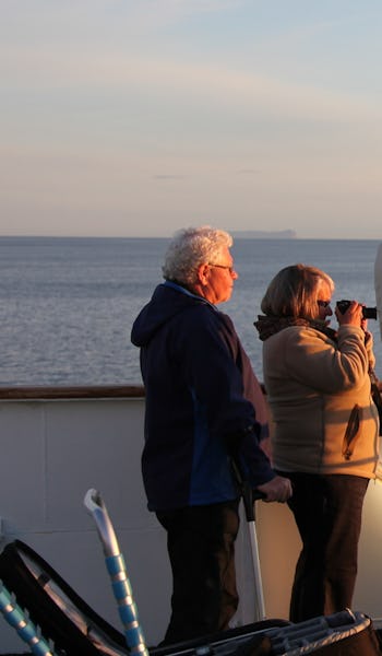 Bilden visar en grupp människor på däck där de tittar på och fotar solnedgången.