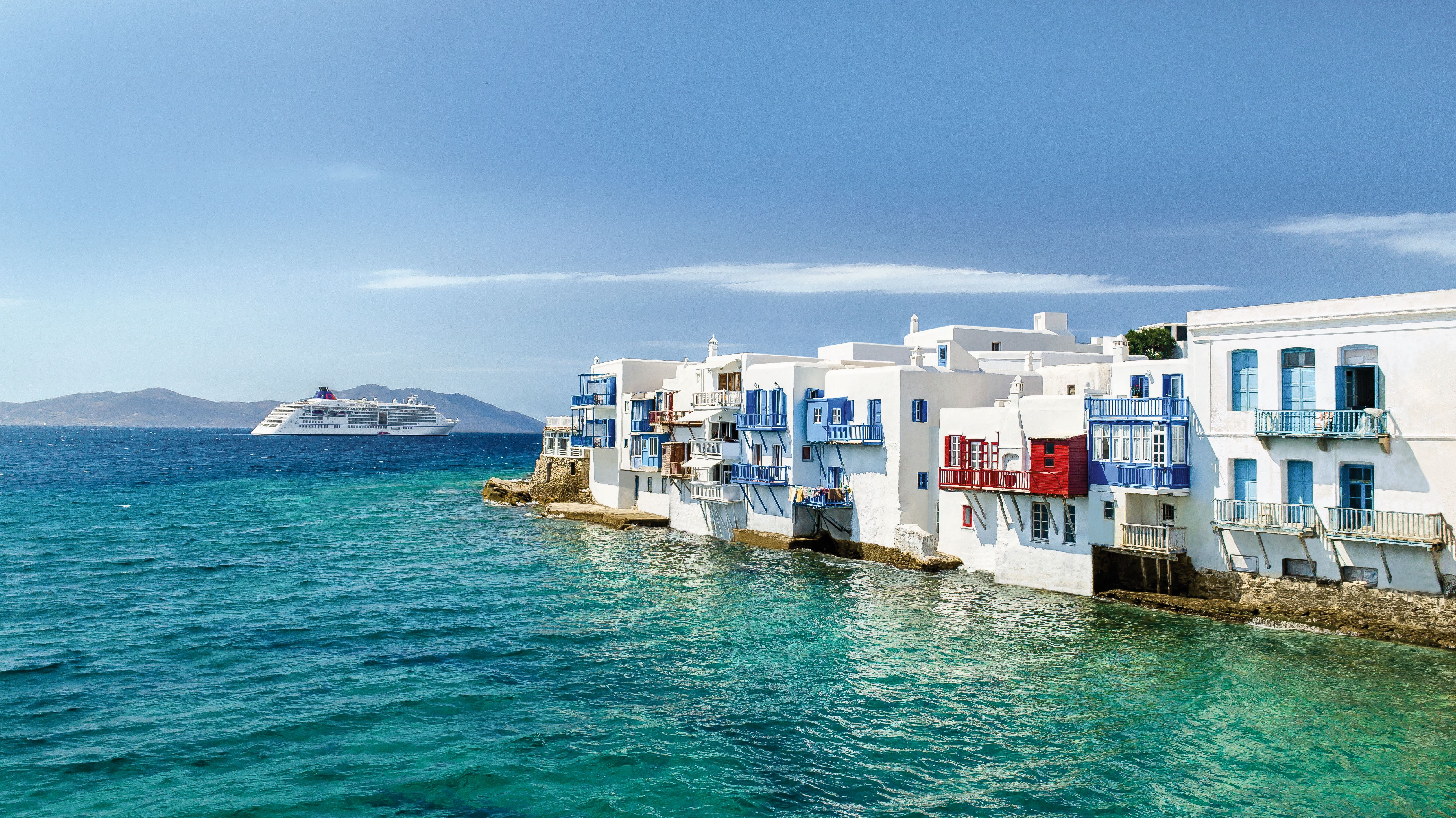 Bilden visar Hapag-LLoyds fartyg i Medelhavet utanför Mykonos kust. På bilden syns turkost hav och vitkalkade hus med blå balkonger och fönsterluckor.