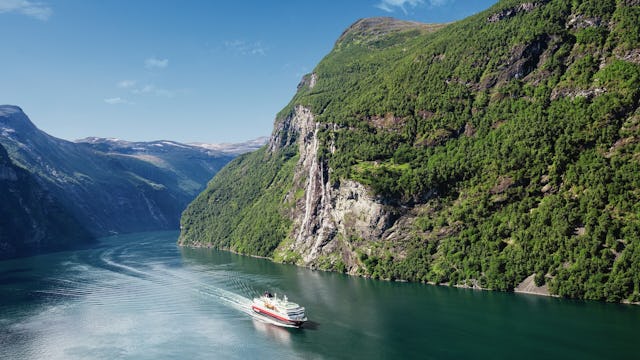 Bilden visar ett av Hurtigrutens fartyg som åker genom Geirangerfjorden.
