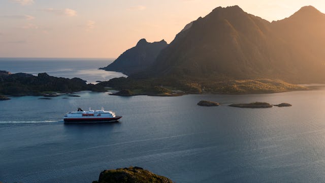 Bild på MS Kong som kryssar i Lofoten. Vackra berg och fjordar i bakgrunden. Kryssa Hurtigruten och upptäck Norges vackra landskap.